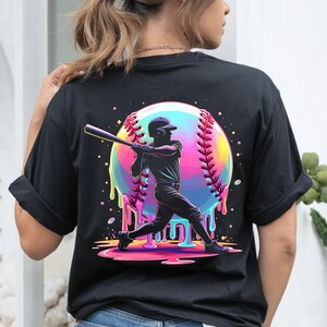 May include: Black t-shirt featuring a colorful baseball design. The graphic shows a baseball player swinging a bat, set against a vibrant, dripping baseball. The baseball has rainbow colors and red stitching. A fun, sporty design.