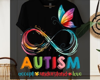 May include: A black t-shirt featuring a rainbow infinity symbol and the word "AUTISM" in rainbow lettering. The text "accept understand love" is positioned below the word "AUTISM". A rainbow butterfly is situated above the infinity symbol. The text "DTG TRANSFER READY TO PRESS" is at the top of the image.
