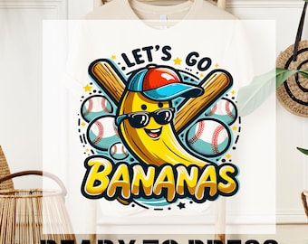 May include: White t-shirt with a cartoon banana wearing a baseball cap and sunglasses, holding two baseball bats. The banana is surrounded by baseballs and the text "Let's Go Bananas".