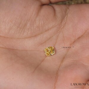 May include: A yellow cushion-cut lab-grown diamond on a person's hand. LABGROWN GERMANY is printed on the hand.