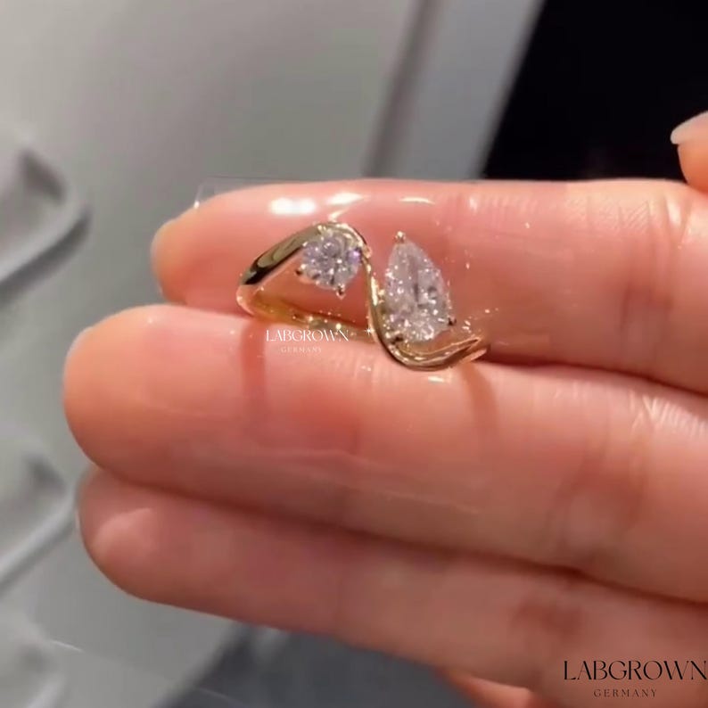 May include: A gold ring with two pear-shaped diamonds set in a unique, twisted design. The ring is on a finger.