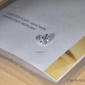 May include: A white card with the text "Laboratory Grown Diamond Report" and the logo "Labgrown Germany". A clear heart-shaped diamond is displayed on the card.