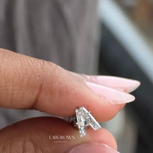 Puede incluir: Primer plano de un pendiente de diamante cultivado en laboratorio con un dise&ntilde;o geom&eacute;trico &uacute;nico. El pendiente presenta una piedra grande, clara, de corte triangular y piedras de acento m&aacute;s peque&ntilde;as. El texto "LABGROWN GERMANY" es visible.