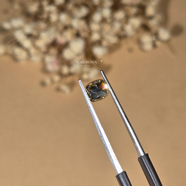 May include: A cushion-cut, light brown lab-grown diamond held by tweezers. The diamond has a slight green hue.