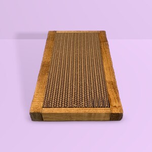 May include: A rectangular scratching post for cats with a brown cardboard scratching surface framed in natural wood.