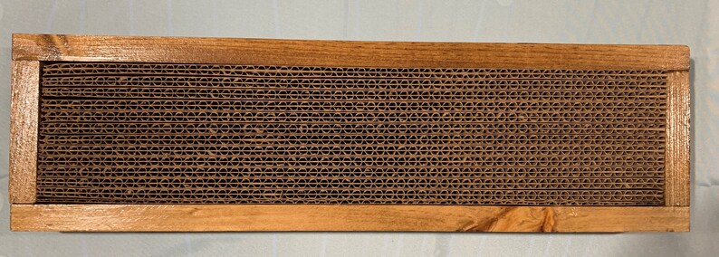 May include: A wooden frame with a brown cardboard honeycomb pattern inside. The frame is made of natural wood and has a rustic look.