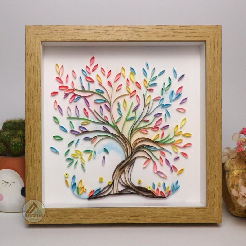 May include: A framed paper art piece depicting a colorful tree with rainbow leaves. The tree is made of paper and is framed in a light wood frame.