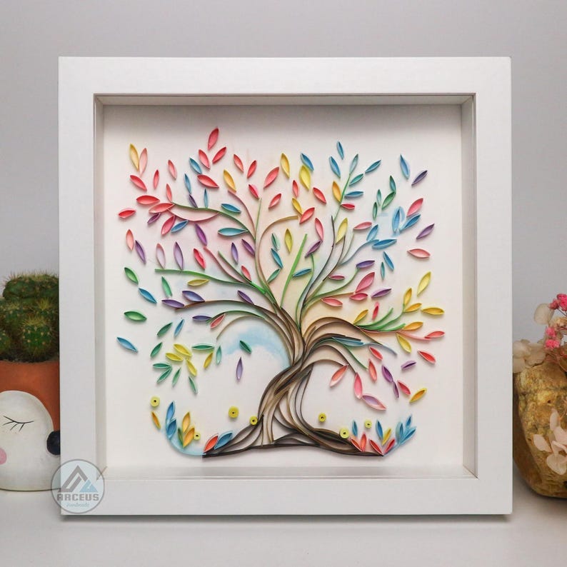 May include: A framed paper art piece depicting a colorful tree with rainbow leaves. The tree is made of curled paper and is set against a white background.