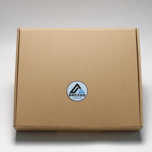 May include: A brown cardboard box with a white circle sticker that says "ARCEUS handmade" in black text. The sticker has a blue and black mountain logo.