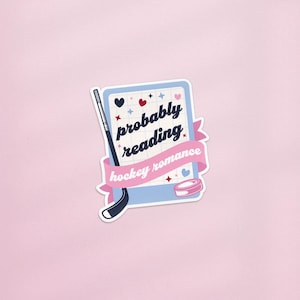 Könnte beinhalten: Ein Aufkleber mit hellblauem Hintergrund und den Worten "probably reading hockey romance" in Schreibschrift. Der Aufkleber zeigt auch einen Hockeyschläger, einen Puck sowie Herz- und Sternakzente. Der Aufkleber befindet sich auf einem rosa Hintergrund.