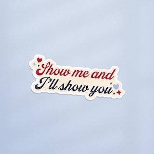 May include: A sticker with the text "Show me and I'll show you" in a retro font. The text is in red and navy blue, with decorative hearts and stars. The sticker has a cream-colored background and a white border.
