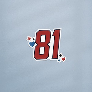 May include: A sticker featuring the number "81" in red with a white outline and a navy blue border. The number is decorated with red, white, and blue stars and hearts. The sticker is on a light blue background.