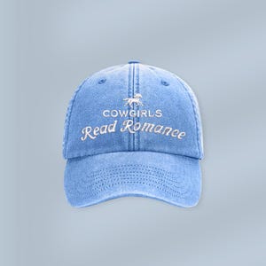Könnte beinhalten: Hellblaue Jeans-Baseballkappe mit dem weißen Schriftzug "COWGIRLS Read Romance". Die Kappe hat einen gebogenen Schirm und eine kleine Pferde-Grafik. Ein lässiges Accessoire.