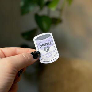 May include: A white sticker with a purple can design. The can has the text "CHAPTER 55" and "TO-MATE-O SOUP" on it.