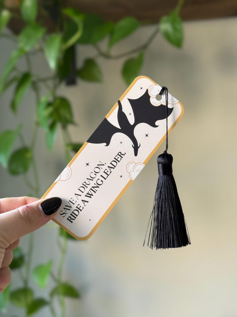 May include: A black and gold bookmark with a black silhouette of a dragon and the text "Save a dragon. Ride a wing leader."