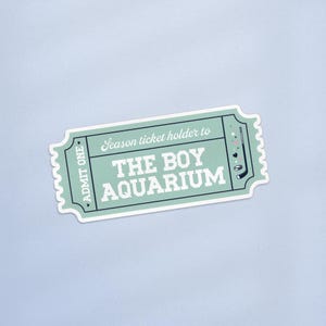 Könnte beinhalten: Ein mintgrünes Ticket mit dem Text "Season ticket holder to THE BOY AQUARIUM" in Weiß. Das Ticket hat einen gezackten Rand und die Worte "ADMIT ONE" auf der linken Seite. Ein Golfschläger und andere kleine Grafiken befinden sich auf der rechten Seite.
