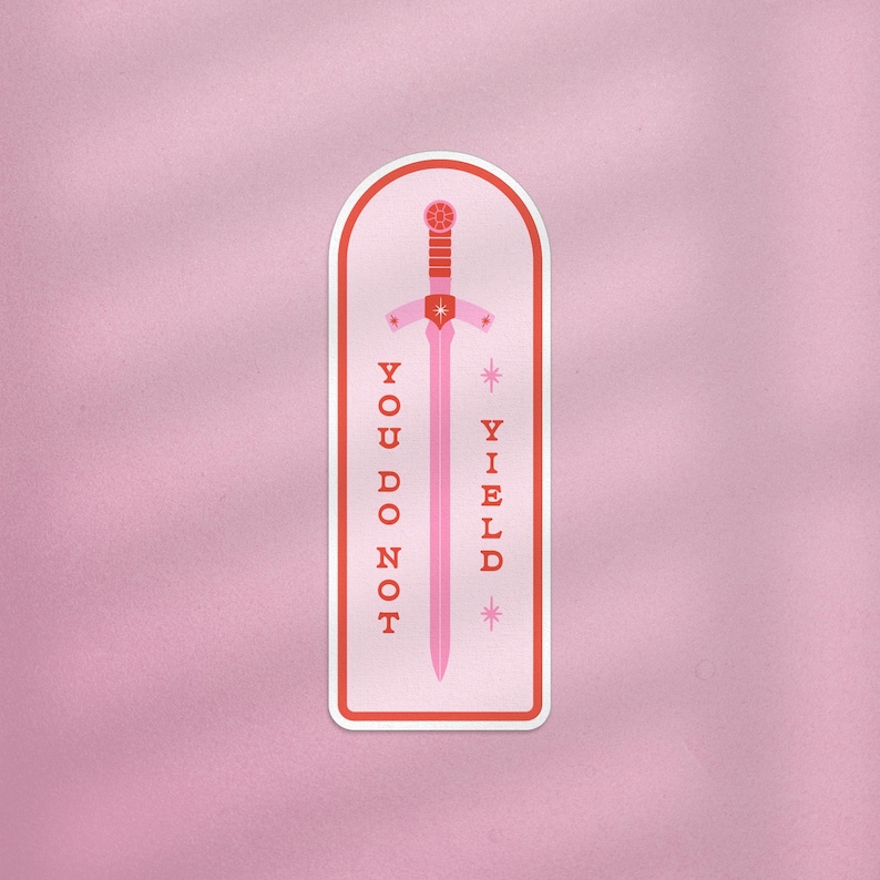 May include: A pink sticker with a sword design and the words "YOU DO NOT YIELD". The sword is pink with a red hilt and a star-shaped design. The sticker has a white border and is set against a pink background.
