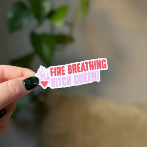 Puede incluir: Una pegatina blanca con texto rosa y rojo que dice "FIRE BREATHING BITCH QUEEN!" con un peque&ntilde;o coraz&oacute;n rosa y un gr&aacute;fico de llama.