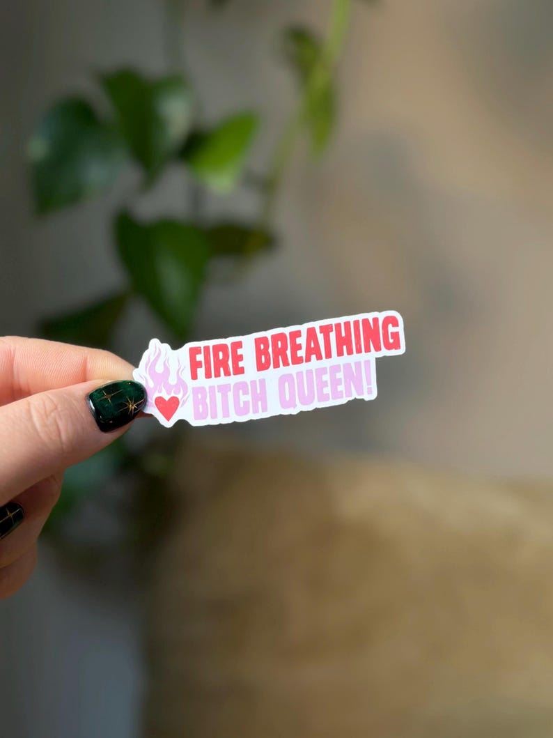 Puede incluir: Una pegatina blanca con texto rosa y rojo que dice "FIRE BREATHING BITCH QUEEN!" con un peque&ntilde;o coraz&oacute;n rosa y un gr&aacute;fico de llama.