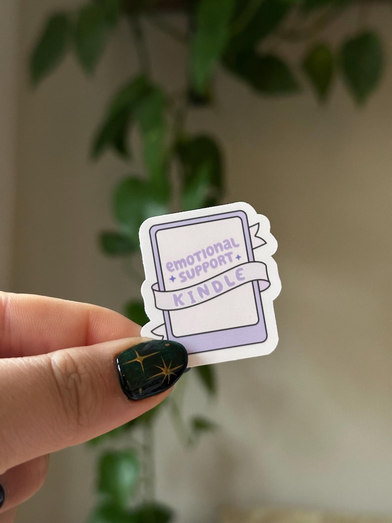 May include: A purple and white sticker with a Kindle e-reader design. The sticker has a banner that reads "emotional support + kindle".