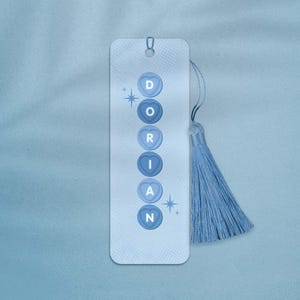 May include: A blue bookmark with a tassel. The bookmark has a white background with a pattern of small dots. The word "DORIAN" is spelled out in white letters on blue heart-shaped buttons.