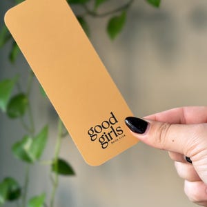 May include: A yellow bookmark with the text "good girls book club" printed in black.