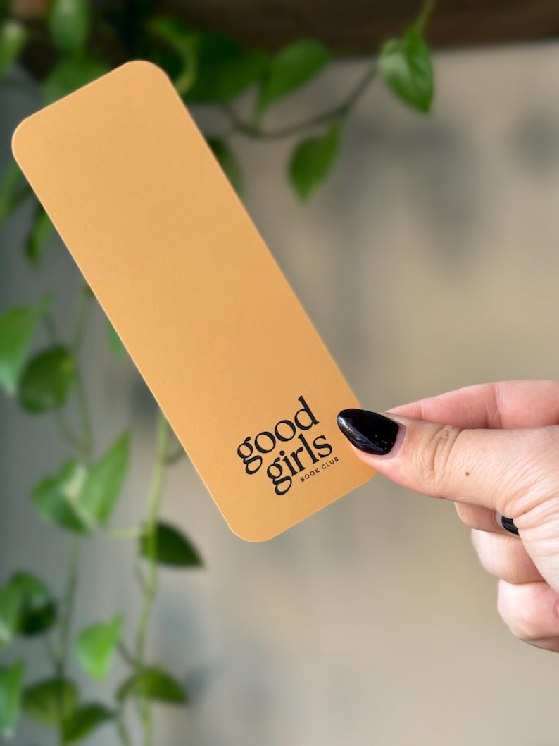 May include: A yellow bookmark with the text "good girls book club" printed in black.