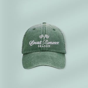May include: A green baseball cap with the text "Sports Romance SEASON" embroidered in white. The cap features a curved brim and a classic six-panel design. Two checkered flags are embroidered above the text.