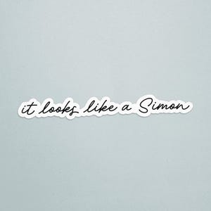 May include: A white sticker with the phrase "it looks like a Simon" in black cursive script. The sticker has a white border and is set against a light blue background.