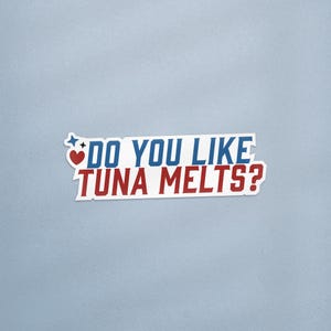 Peut inclure: Un autocollant rectangulaire avec le texte "DO YOU LIKE TUNA MELTS?" en bleu et rouge, avec un cœur et une étoile. L'autocollant a une bordure blanche et est posé sur un fond bleu clair.