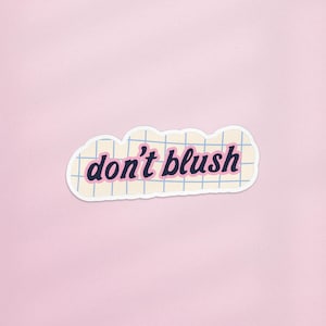 May include: A sticker with the phrase "don't blush" in a retro font. The text is dark blue with a pink outline, set against a cream-colored background with a grid pattern. The sticker has a white border and is set against a pink background.