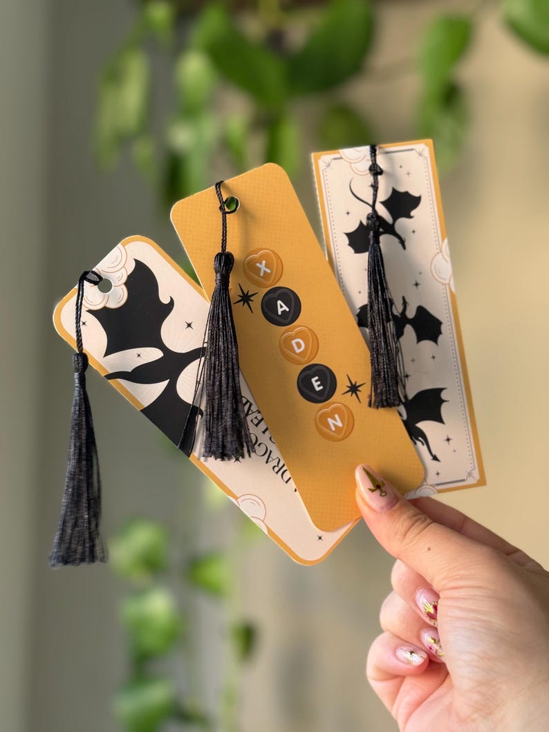 May include: Three yellow and white bookmark designs with black dragon silhouettes and black tassels. The bookmarks feature the text "Dragon Slayer" and black buttons with the letters "X", "A", "D", "E", and "N".