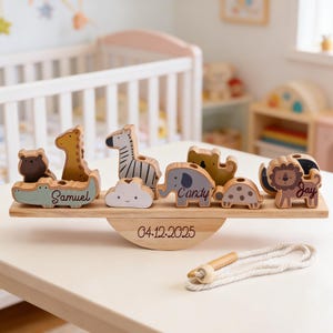 May include: A wooden animal seesaw toy in light wood. It features a bear, giraffe, zebra, cloud, elephant, turtle, and lion. The names "Samuel", "Candy", and "Jay" are inscribed. The date "04.12.2025" is also inscribed on the toy.
