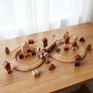 May include: Wooden toy train set with a track, buildings, trees, and signs. The train is brown and beige, and the buildings have red and beige roofs. The track is a light brown color, and the trees are dark brown.