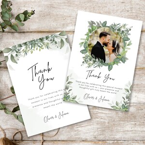 May include: Two white wedding thank you cards with green foliage and the words "Thank You" in elegant script. One card features a photo of a couple. The text reads "Thank you for celebrating this special moment..."