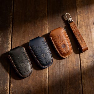 May include: Three leather key fob covers in black, navy blue, and brown, with a matching leather keychain. The key fobs have embossed button details and are stitched with contrasting thread. The keychain is stamped with the word "FERRON".
