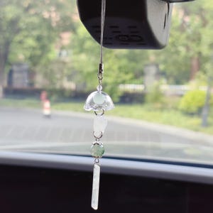 May include: A car charm featuring a clear, jellyfish-shaped pendant with a light green orb and a long, rectangular crystal. The charm hangs from a silver chain, adding a touch of elegance to any vehicle's interior.