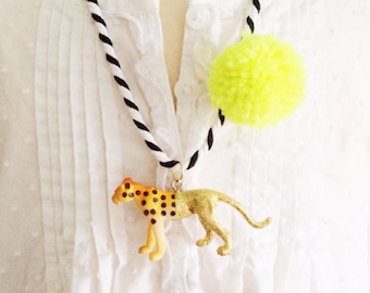 May include: A black and white striped cord necklace with a yellow pom-pom and a gold and black cheetah figurine pendant.