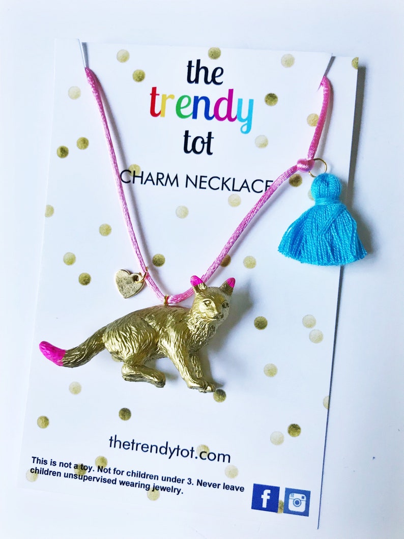 Kids gold cat necklace with pink string, blue tassel and gold heart charm.