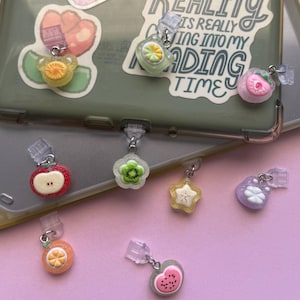 May include: A collection of small, colorful fruit-themed charms with clear plastic clips. The charms feature designs including a yellow citrus slice, a green kiwi flower, a pink strawberry, a red apple slice, a yellow star, a purple flower, an orange slice, and a pink watermelon slice.