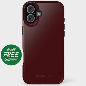 May include: A burgundy phone case with a raised camera bump and the word "Jacqueline" printed on the back.