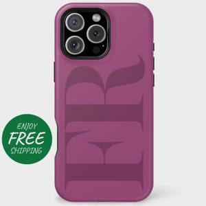 May include: A magenta phone case with a large, stylized "FR" design in a darker shade of magenta. The phone case has a black border and a green circle with the words "ENJOY FREE" in white.