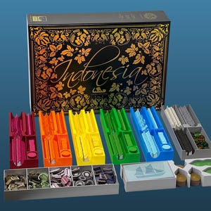 Puede incluir: Una caja de juego de mesa titulada Indonesia Third Edition con patrones ornamentales en negro y dorado, acompañada de varias bandejas de plástico en rojo, naranja, amarillo, verde, azul y gris, que contienen fichas, cartas y marcadores.