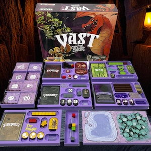 Puede incluir: Juego de mesa "Vast: Crystal Caverns" con una caja que muestra un dragón rojo y criaturas verdes. Las bandejas moradas contienen cartas, fichas y piezas de juego. El juego incluye el texto "Sidequest" y "The Knight".