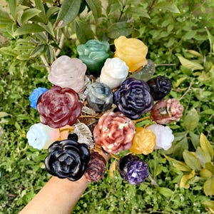 May include: A bouquet of rose-shaped crystal flowers in various colours, including pink, red, purple, green, yellow, and black. The flowers are arranged on gold stems and have a natural, organic look.