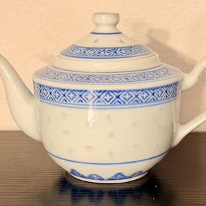 Puede incluir: Tetera de cerámica blanca con un patrón geométrico azul alrededor del borde y la tapa. La tetera tiene un pico y un asa curvos, y un pequeño pomo en la tapa. El diseño es de estilo asiático clásico.