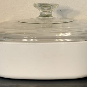 Può includere: Una pirofila rettangolare bianca con coperchio in vetro trasparente. La pirofila ha due manici ed è progettata per l'uso in forno. Il coperchio ha un pomello in vetro trasparente. Questo utensile da cucina è adatto per cuocere e servire.