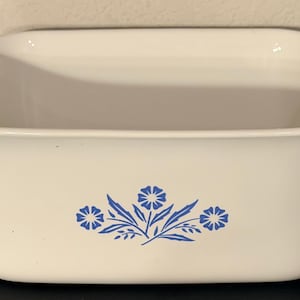 May include: White rectangular baking dish with two handles. The dish features a blue floral design on the front. The dish is approximately 20 cm wide and 20 cm long.