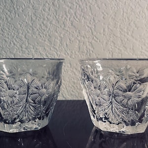 May include: Two clear glass cups with a floral pattern. The cups have a handle and are made of cut glass.