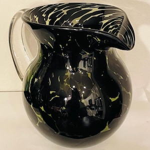 May include: A black glass jug with a clear handle and spout. The jug features a pattern of light green and white swirls and spots. The jug is a decorative item.